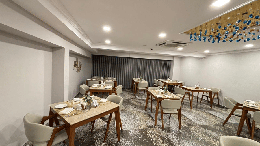 Elegant restaurant at Biznotel by Pride Surat with neatly set wooden tables and comfortable beige armchairs.