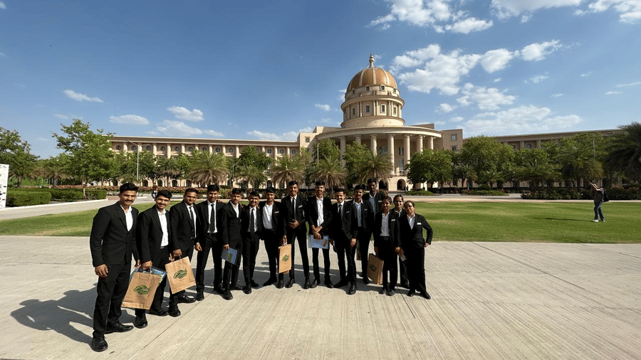 A group of people stands outside the college building. They pose together on a pathway next to a lawn.