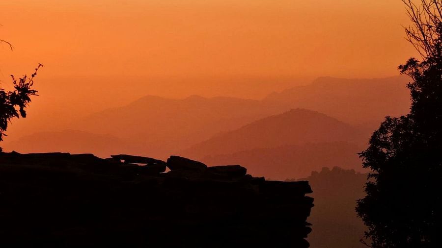  A breathtaking sunset view, with silhouetted trees framing the layered mountain ranges, showcasing the natural beauty and tranquility of the surrounding landscape, possibly captured from the resort
