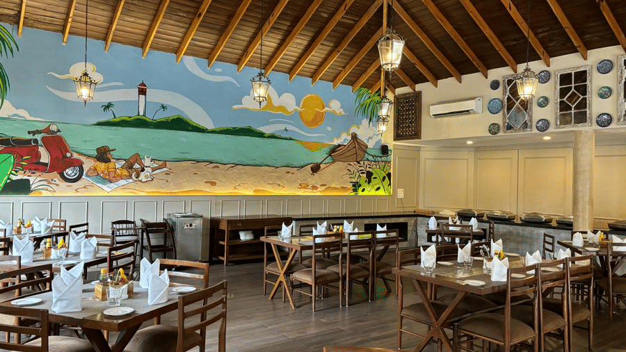 Full view of the Tulipe All-day Dining Restaurant featuring wooden chairs and tables set in the dining space, along with a wall mural inspired by the Goan beaches - Golden Tulip Goa Mandrem