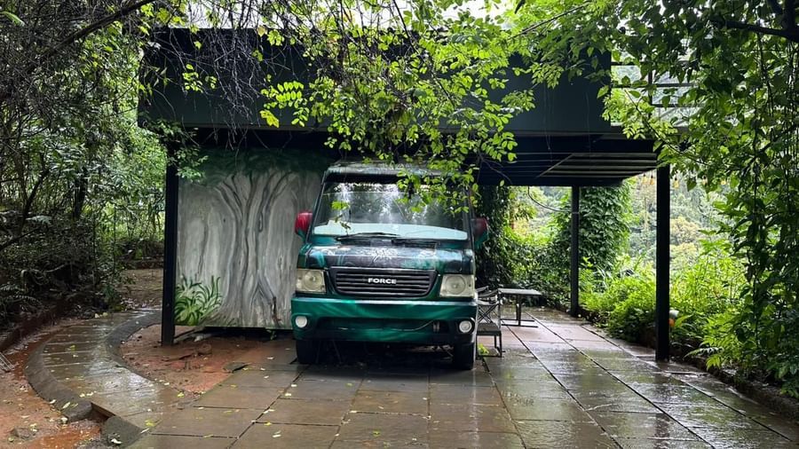 Natural stone driveway with classic green vehicle surrounded by lush rainforest vegetation at Holistic Eco-Resort, Kannur Retry