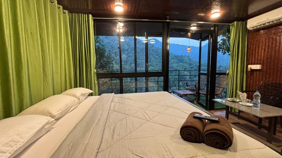 Serene meditation space with hardwood flooring, floor-to-ceiling green curtains, and bolster pillow at Holistic Eco-Resort, Kannur.