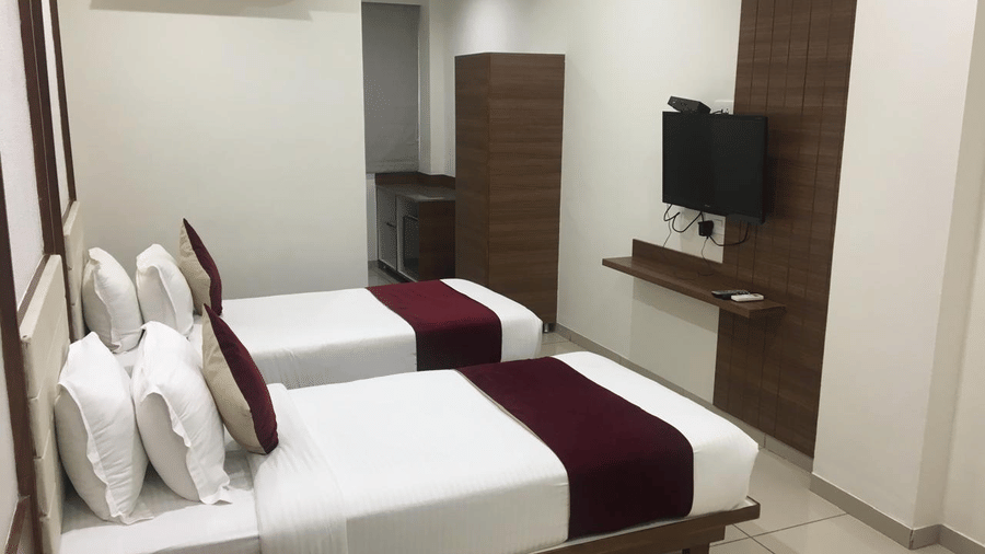 A Deluxe Room at Hotel Ashray Inn Express featuring a large bed with side tables, wall-mounted television, wardrobe, and modern interiors