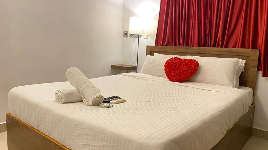 A bed, with bedding and a heart shaped cushion, with a side lamp beside the bed in a bedroom | La Paradise Residency, Pondicherry