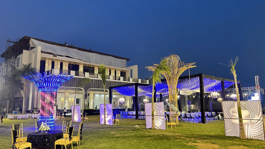 Pride Premier Alwar | An event space with illuminated decorations, chairs, trees, and the building.