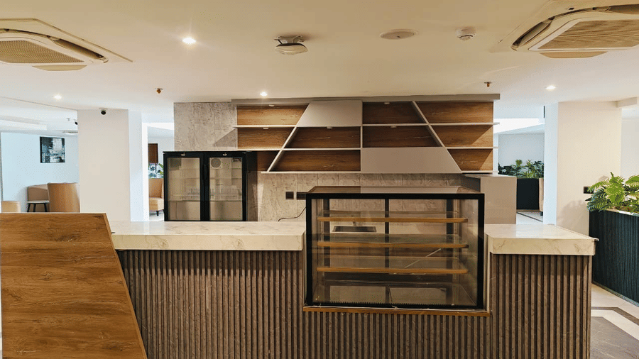 Front view of the Mr. Confectioner bakery counter at Pride Premier Greater Noida, featuring wood panelling and glass display cases in the lobby.
