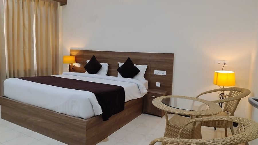 Deluxe Room at Pride Resort Rudraprayag featuring a queen size bed with wooden headboard and lamps on both sides and sitting space showcasing a pair of chairs and a coffee table next to it
