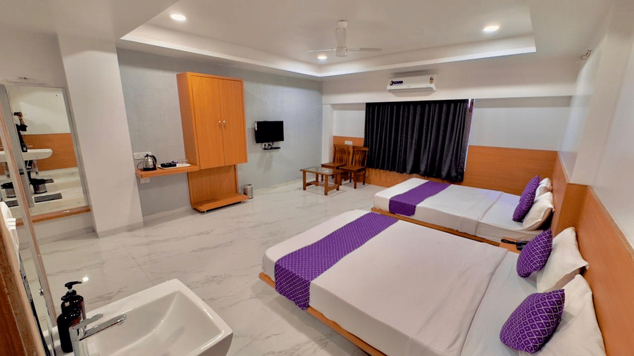 Spacious guest room at Pushpak Resort, Shirdi, featuring two large beds, a TV, and a seating area.