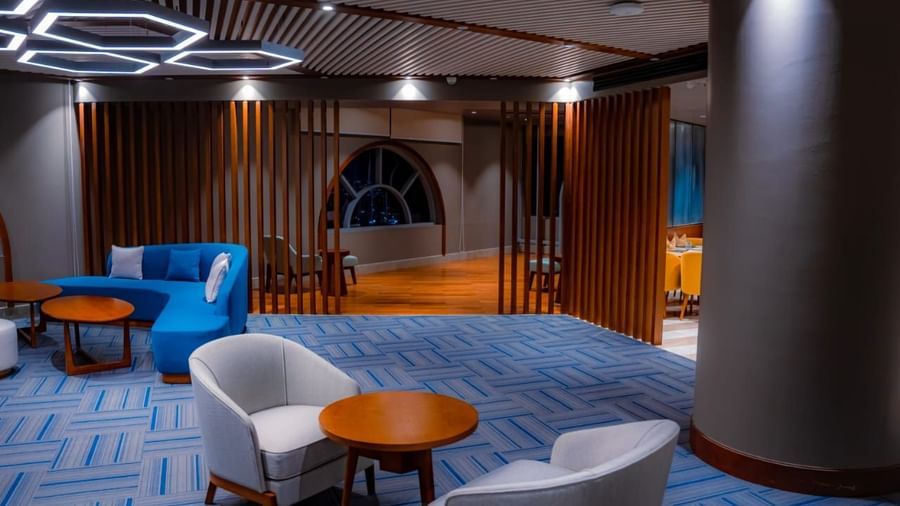 A dining area in Hargeisa with over the head glowing ring lights, wooden partitions, and plush blue sofas - Serene Sarovar Premiere Hargeisa