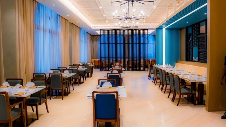 A spacious restaurant interior with modern lighting and long rows of tables - Serene Sarovar Premiere Hargeisa
