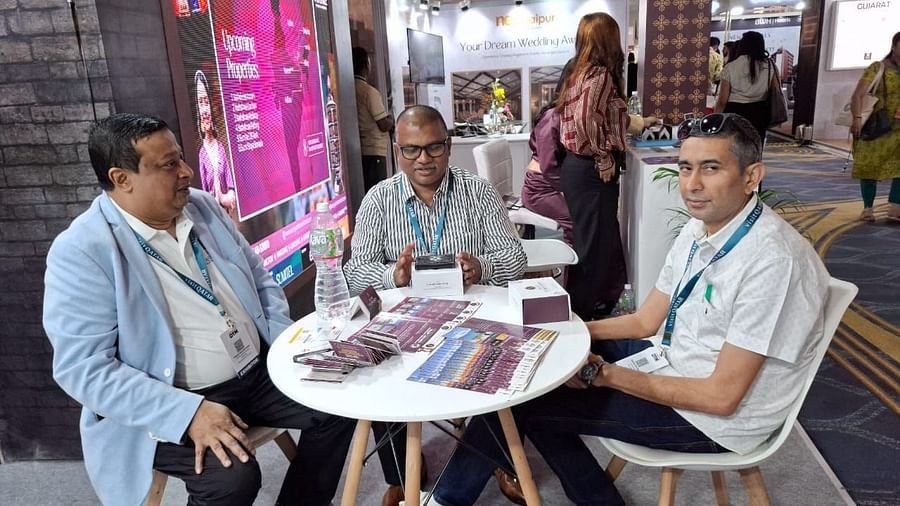 Three individuals seated at a table at the Sumi Yashshree Hotels & Resorts booth, engaged in a professional discussion surrounded by event displays.