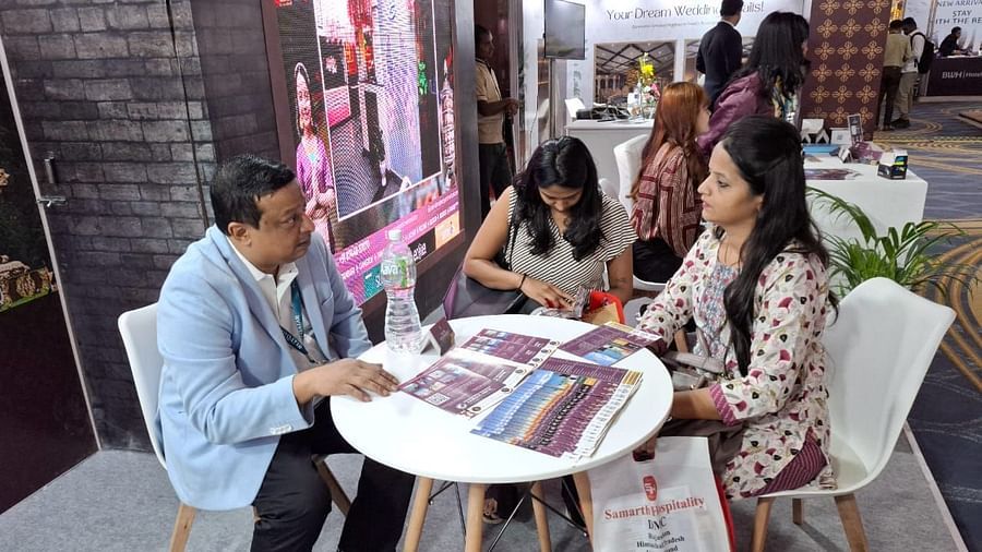 Two women and a man having a focused discussion at the Sumi Yashshree Hotels & Resorts booth, with promotional materials displayed on the table .