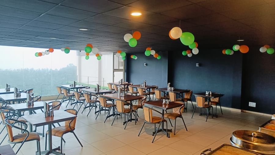 Indoor dining hall decorated with colorful ceiling accents and large windows overlooking the hills at The Cliff Edge Coorg Hotel.