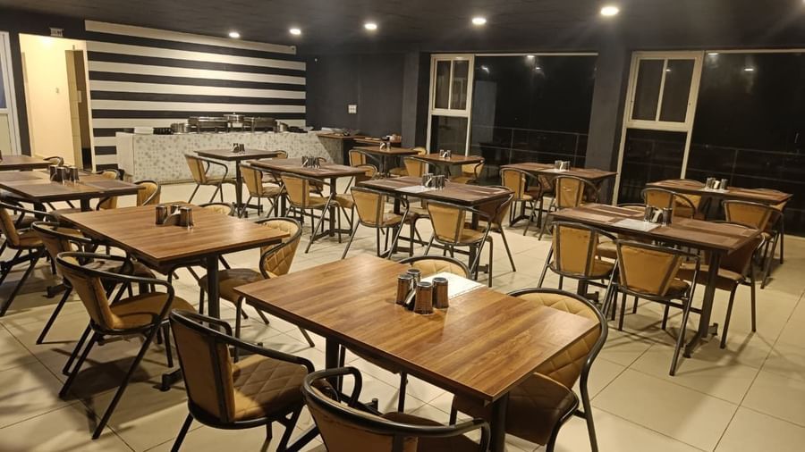 Spacious indoor restaurant with neatly arranged wooden tables and modern lighting at The Cliff Edge Coorg Hotel.