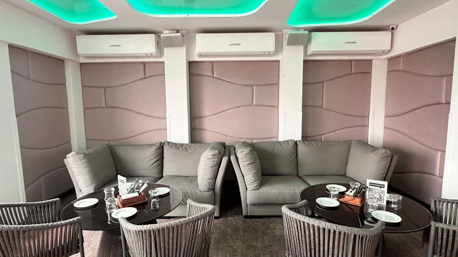 Modern indoor lounge area featuring comfortable grey sofas, armchairs, and distinct green ceiling lighting.