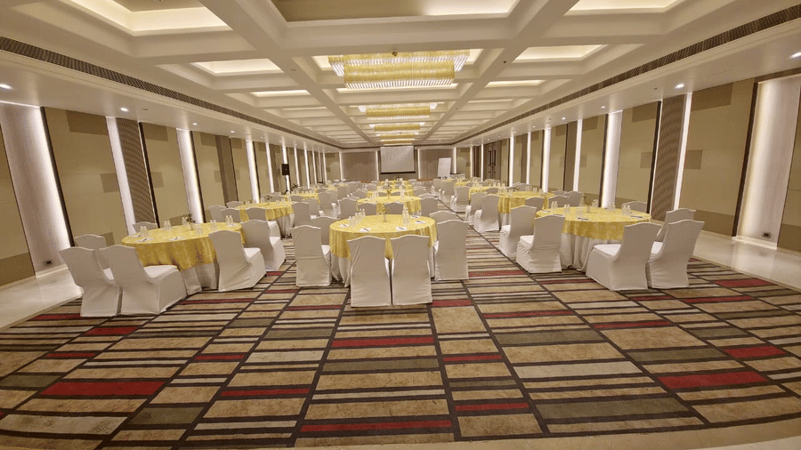 Expansive banquet hall at The Piccadily with yellow-draped round tables, white chair covers, striped carpet flooring, and elegant coffered ceiling lighting.