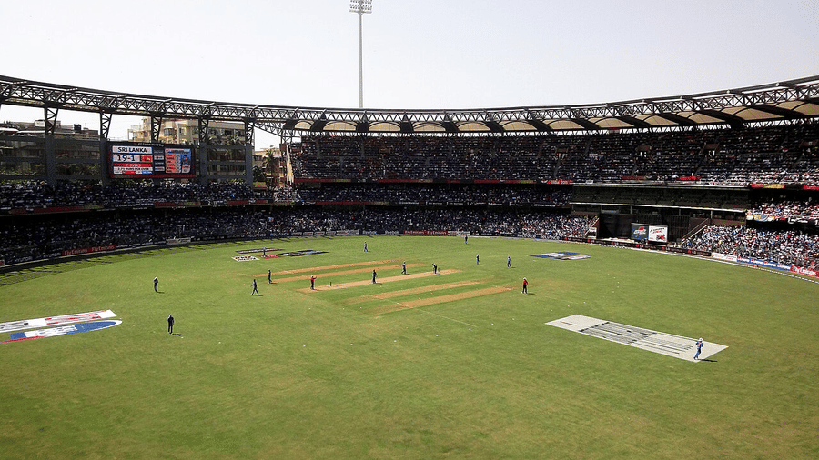 Match underway in a large stadium, players warming up near the pitch while spectators watch from the curved stands.