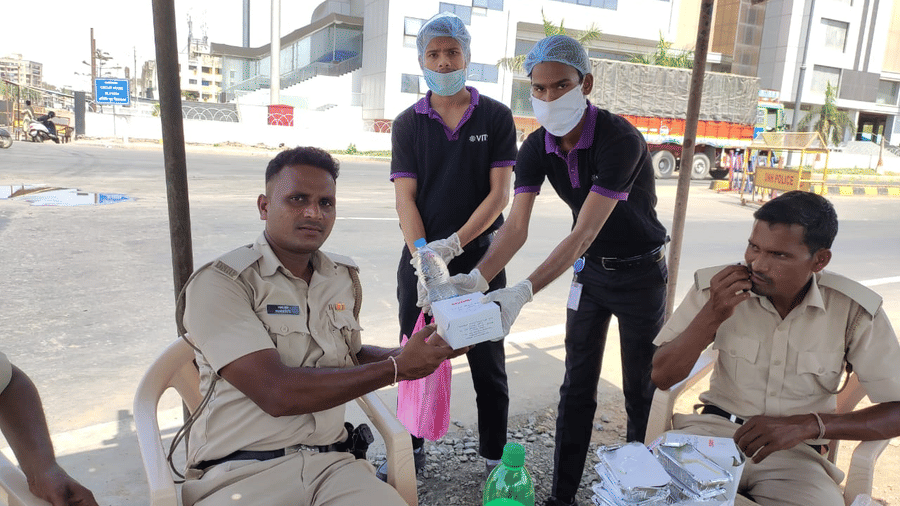 two staff members of giving a snack box to the police while posing for a picture - VITS Hotels & Resorts