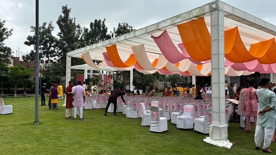 A wide view of a wedding celebration with arranged tables, chairs, and festive canopies in an open lawn area.