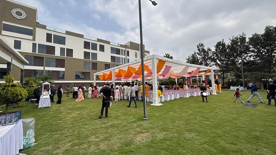 A wide view of a wedding celebration with arranged tables, chairs, and festive canopies in an open lawn area.