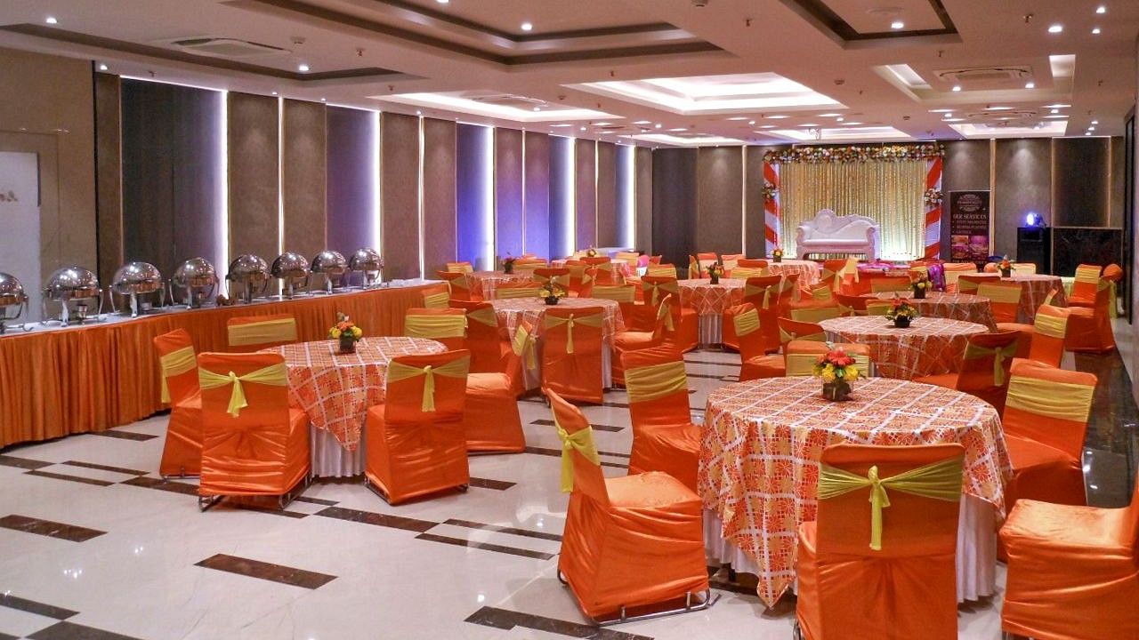 Banquet hall at Hotel Saket 27 with organised tables and chairs in orange decor.