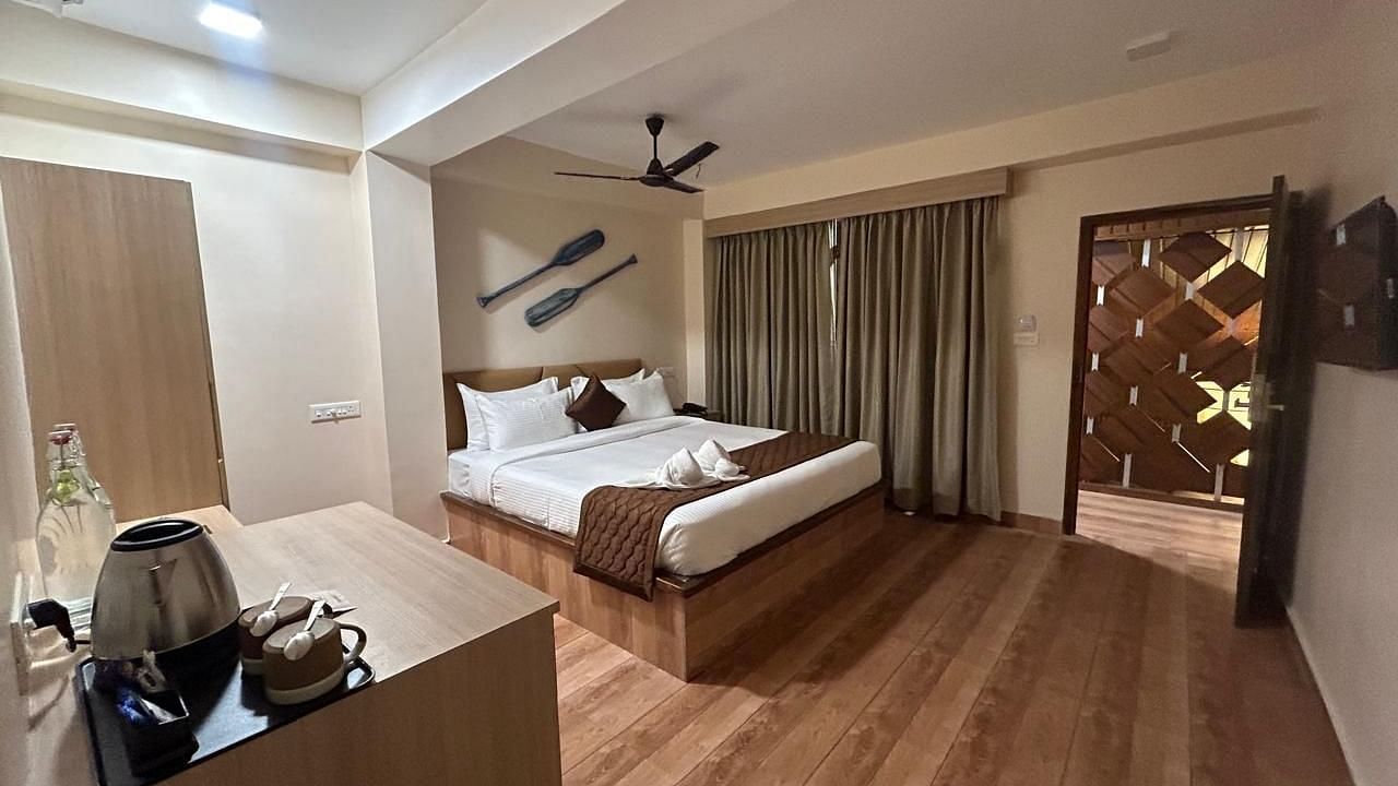 Image of  a room at the resort with a king size bed, wooden flooring and wall mounted decor along with a side table with electric kettle  | Arina Island Resort