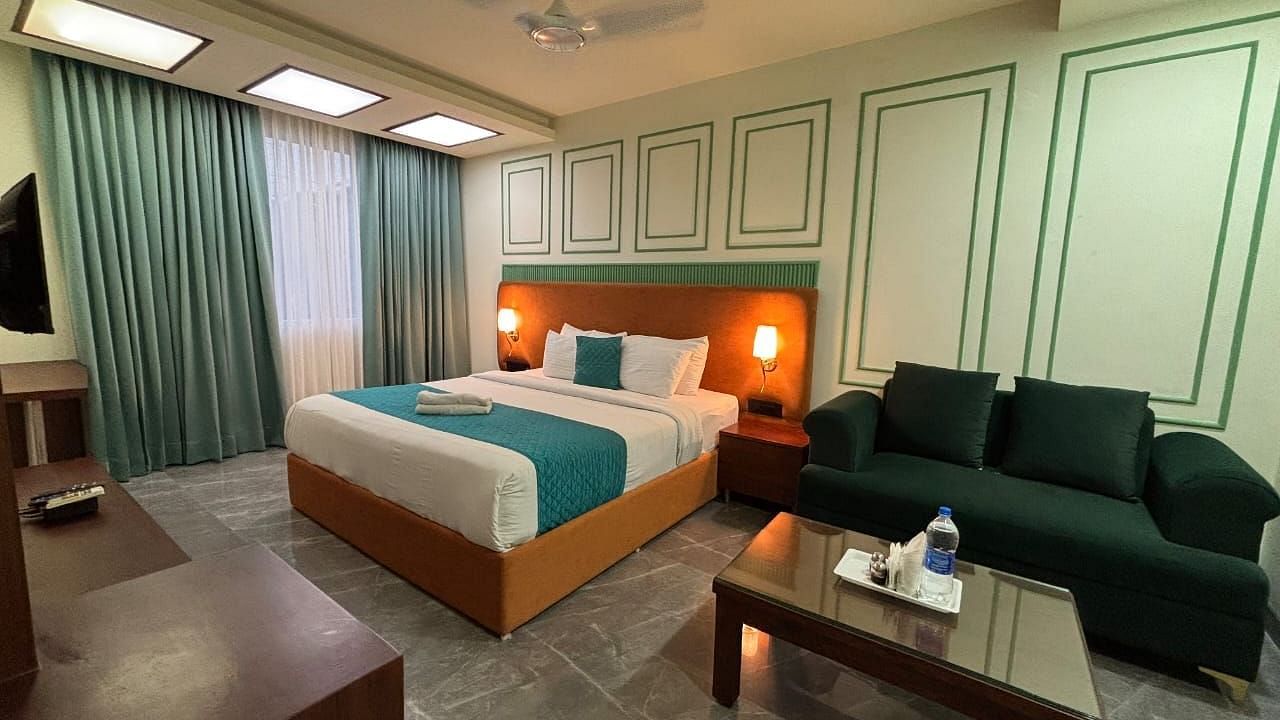 A spacious room with a double bed, a dark green sofa, and a wooden coffee table - Asian Suites IFFCO Metro, Gurgaon
