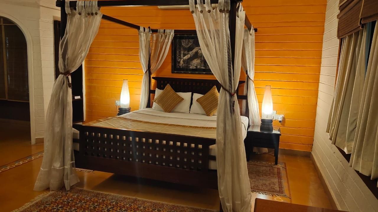 An overview of a plush queen size bed with white poster curtains in the heritage suite room at hoysala village resort, hassan.