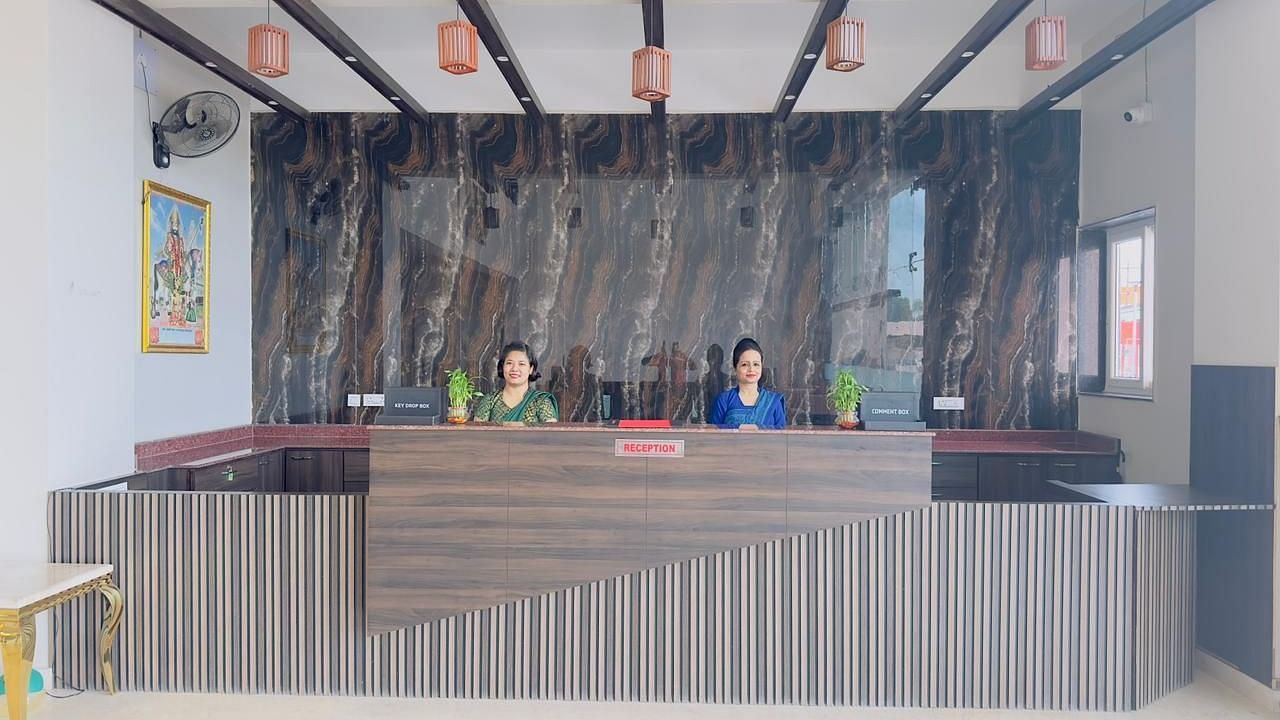A reception desk with a striped front and wooden beams above is attended by staff - Kankidham Lords Inn
