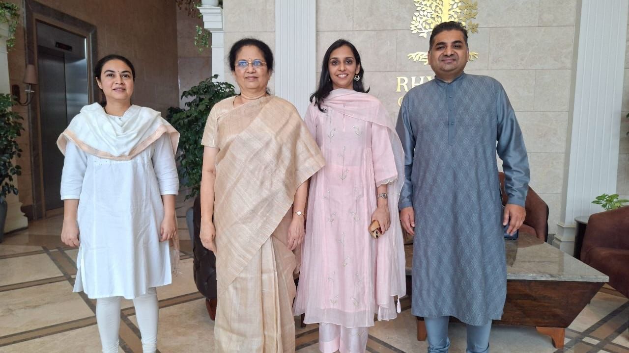 Group photo of four people in traditional attire standing in the lobby of Rhythm Hospitality with the hotel logo in the background.
