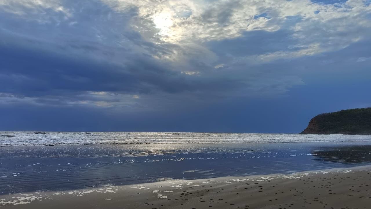 A calm ocean scene with waves breaking on a rocky shore beneath a dramatic, cloudy sky - Cabana