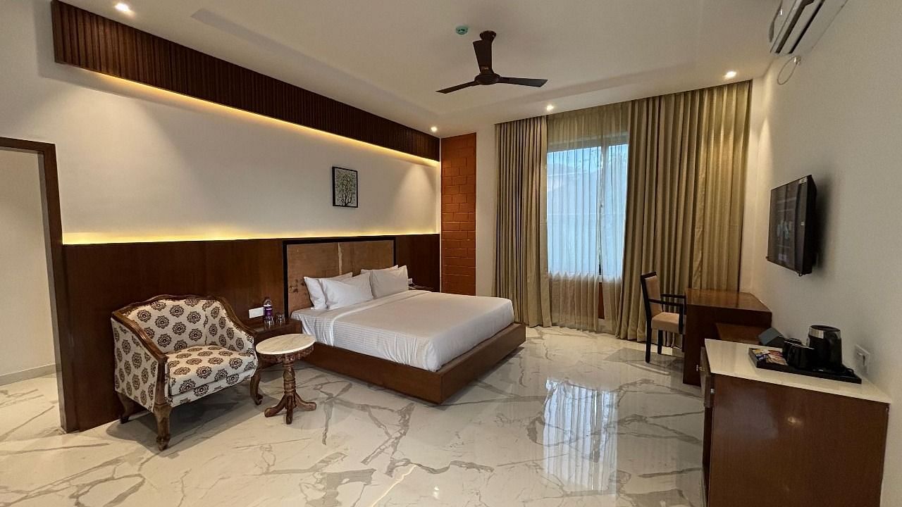 A bedroom with double bed, chair, round table, TV, desk at A room with double bed, framed wall art, fan, round table with chairs at A room with double bed, framed wall art , round table with two chairs at side at Trishvam Symphony, Krishnagiri.