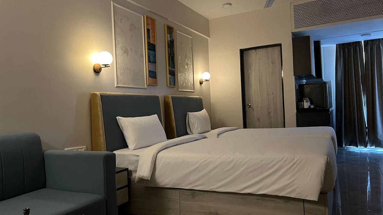 A side view of the spacious room featuring twin beds, a wall-mounted night lamp, and a photo frame above the headboard at Urban Suites by BluSalzz, Jaipur.