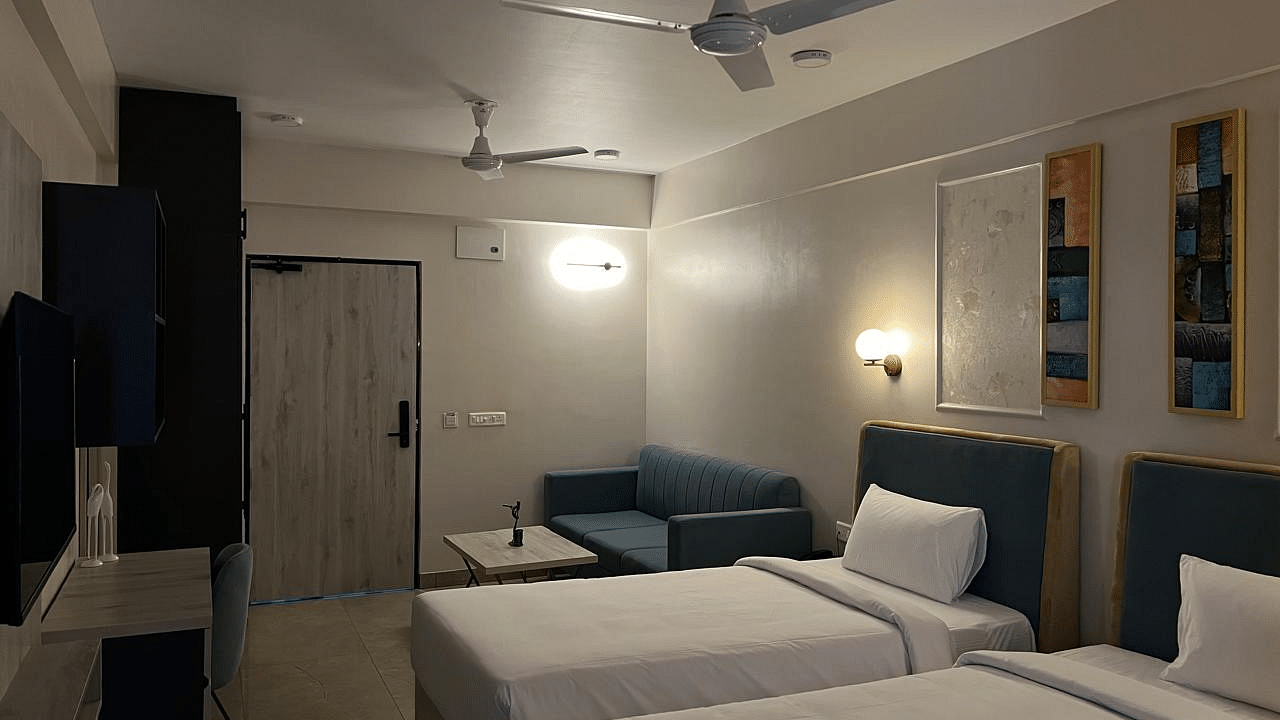 A spacious room featuring twin beds, a wall-mounted TV opposite them, and furniture with a table beside the door at Urban Suites by BluSalzz, Jaipur.