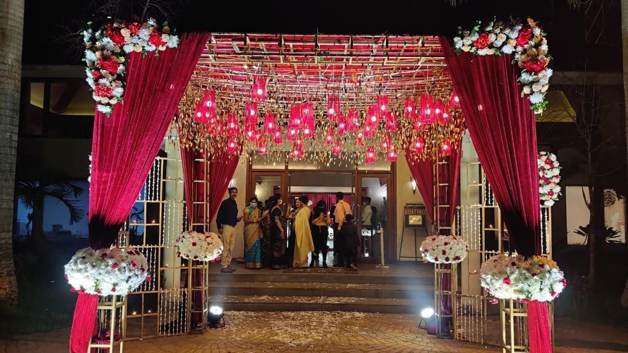 A vibrant red and gold wedding mandap with floral decorations and glowing lights stands as an inviting entrance