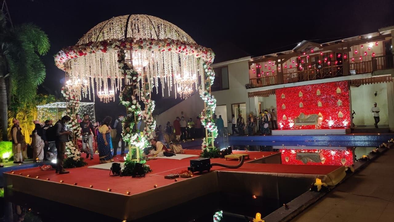 A circular, elaborately decorated mandap with hanging floral elements is set up outdoors for a wedding ceremony