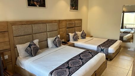 A hotel room featuring two beds side by side, each with a striped bedspread, and a small painting on the wall.