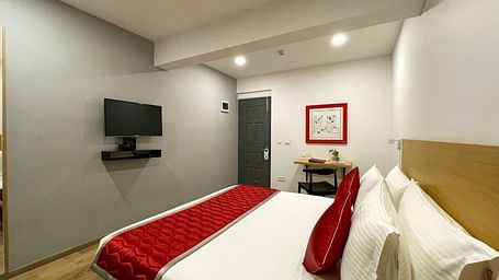 A bedroom featuring a double bed featuring a red and white bed runner along with a wall mounted television on the wall - Lords Eco Inn Belagavi
