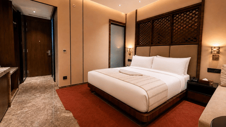 Loom room at Ni Central Park featuring a king bed, warm headboard accent, and carpeted flooring.