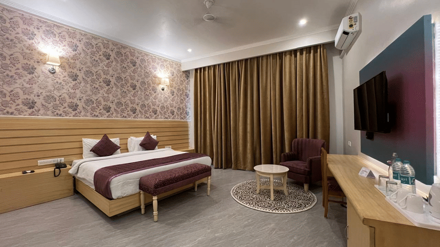 A bedroom with a double bed, patterned wall, TV, and seating area at A S Hotels, Khajuraho.