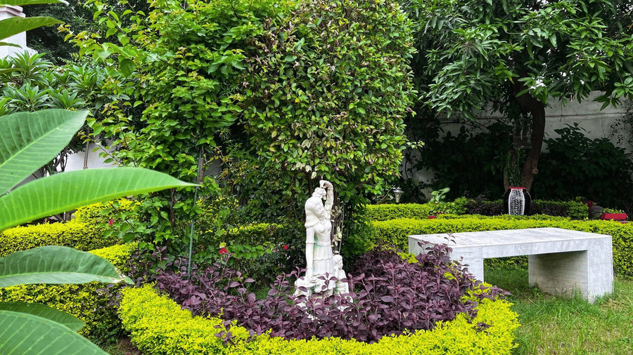 A garden area with a statue, plants, and a stone bench at AS Hotels, Khajuraho.