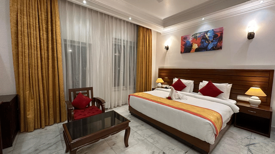 A bedroom with a double bed, chairs, curtains, and wall art at AS Hotels, Khajuraho
