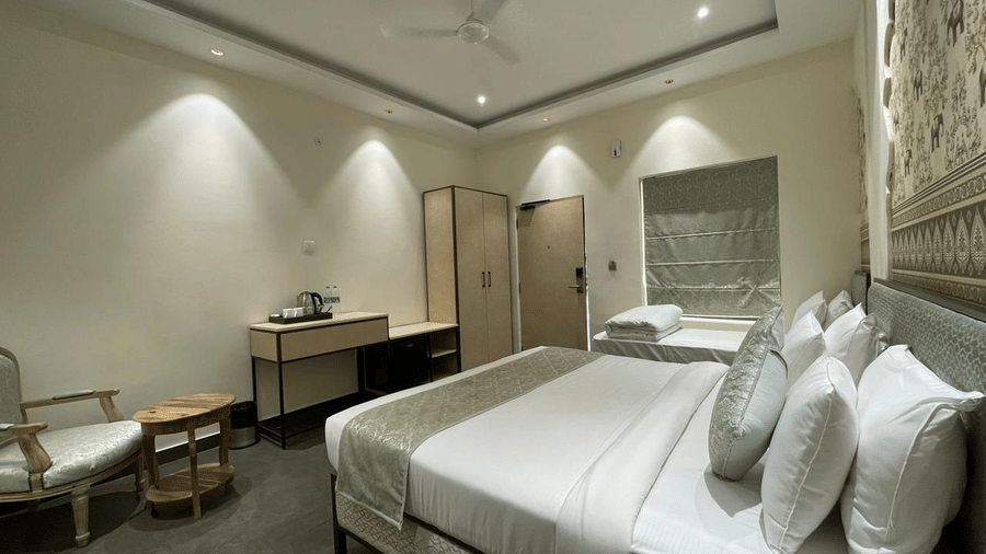 A bedroom at Beelwa Palace,Jaipur, featuring 2 single beds, a table, desk, cupboard, and an armchair.
