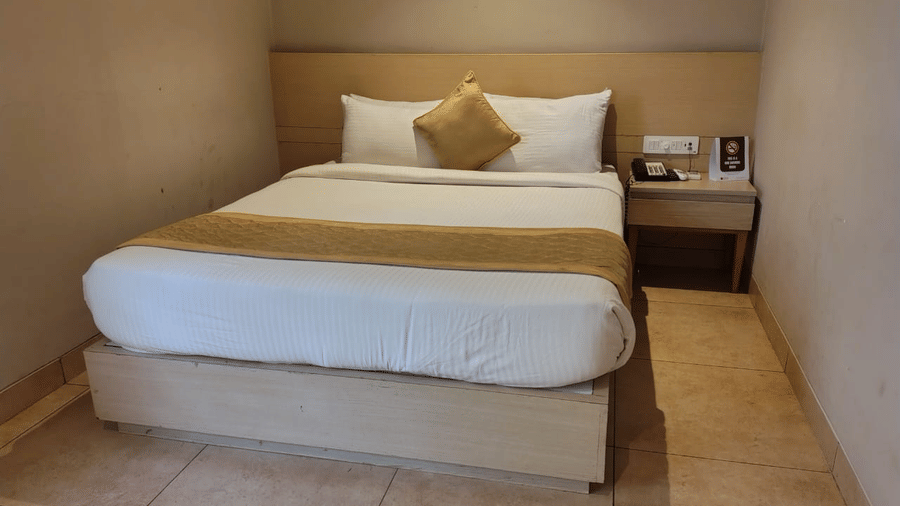 Standard Room at Cholaa Dynasty, Kumbakonam featuring a double size bed and a bedside table which has a telephone and few remotes.