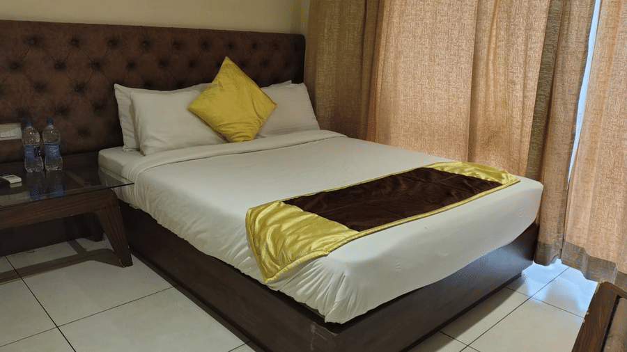 Lawn View Room at Cholaa Dynasty, Kumbakonam featuring a double size bed and a bedside table with two mineral water bottles.