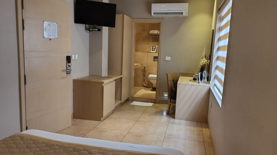 Interiors of the Lawn View Room at Cholaa Dynasty, Kumbakonam featuring a bed, flat TV screen, AC, cabinet tables, and a workstation.