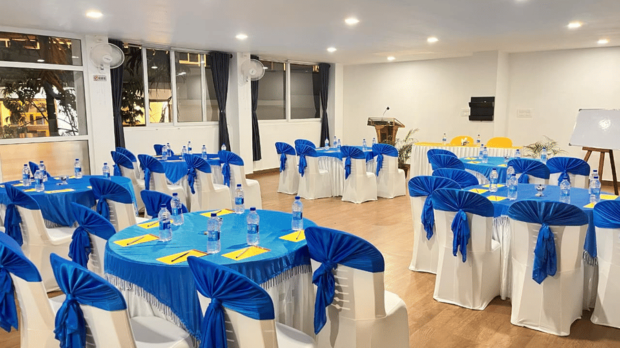 A large indoor event hall set up with many round tables and chairs, all decorated with bright blue and yellow cloth coverings at Coorg Orange Blossom Resort and Spa.