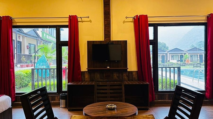 View of the dining table placed in front of a TV with outdoor views on either sides in Family Cottage at DLS MJ River Resort, Rishikesh.