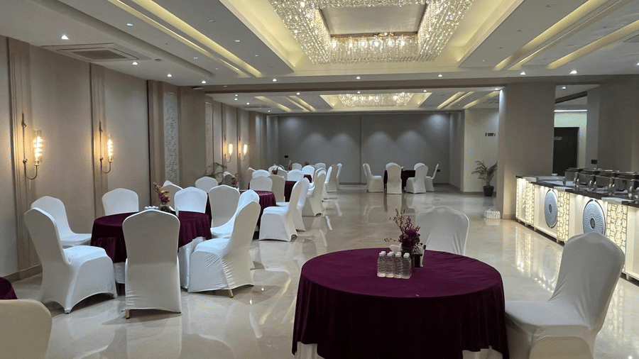 Round tables with a magenta table cloth along with chairs neatly arranged under the elegant false ceiling of the Sapphire Hall at Hotel 91 Privé, Gurugram.