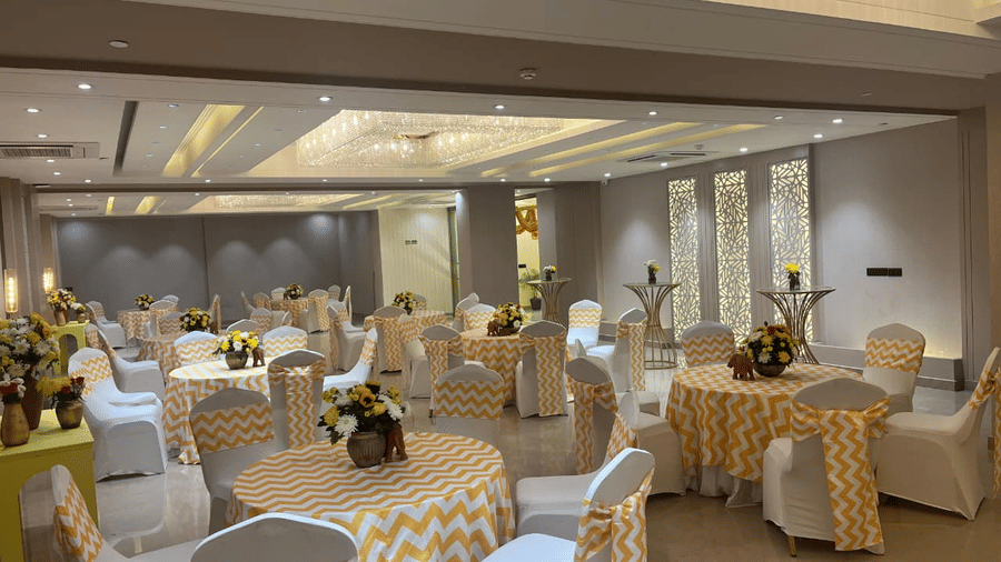 A beautifully decorated Sapphire Hall at Hotel 91 Privé, Gurugram, featuring a vase full of white and yellow flowers placed on each table.